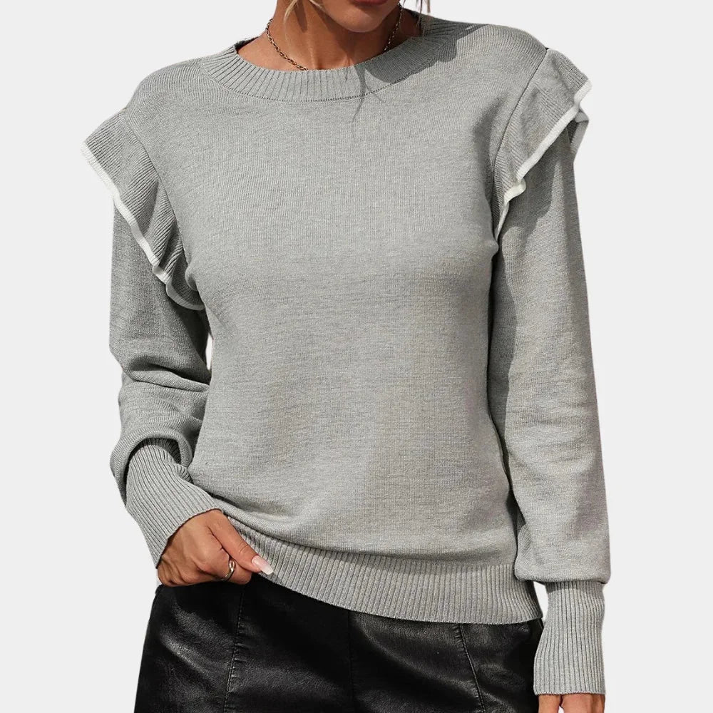 Grey ruffle-trimmed crewneck sweater by Brea. Soft knit fabric with elegant ruffle detailing along neckline, capturing a…
