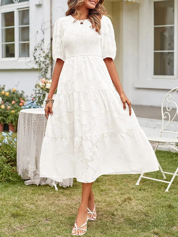 White midi dress with floral textured patterns and tiered design by Emily. Made of lightweight and breathable fabric.