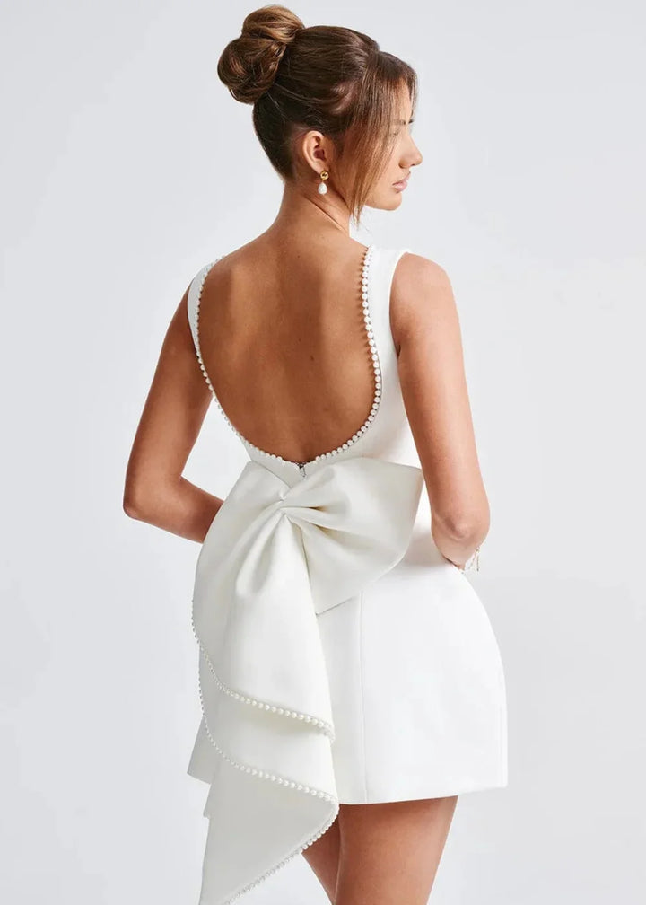 White backless mini dress with bow detail, made from soft and stretchy fabric. Perfect for a chic and elegant look.