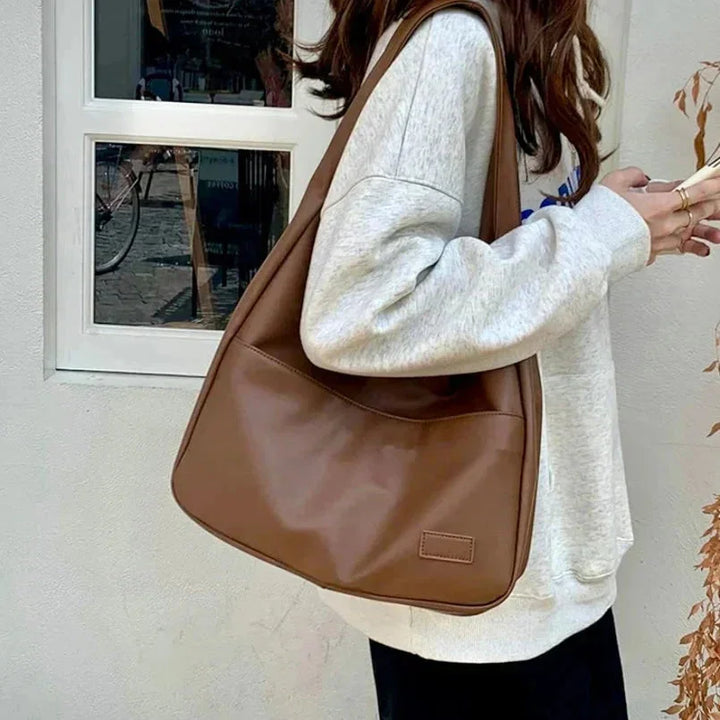 Black faux leather shoulder bag with clean lines, adjustable strap, and gold hardware accents by Candy.